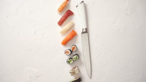 varios rollos de sushi con cuchillo japonés sobre fondo de pizarra de piedra blanca