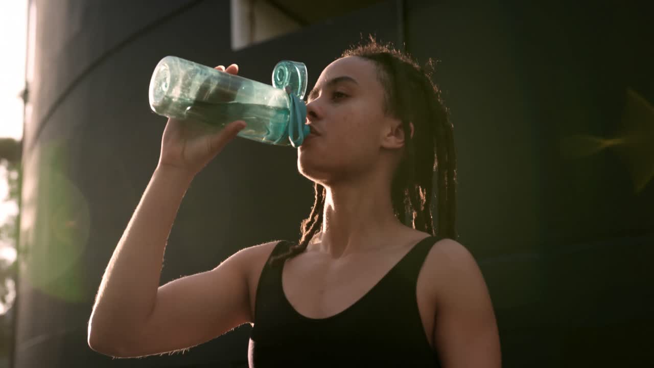 vista frontal de una joven mujer afroamericana bebiendo agua en la ciudad 4k