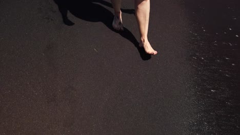 a shot focused on woman´s feet with red painted nails walking on a black sand beach