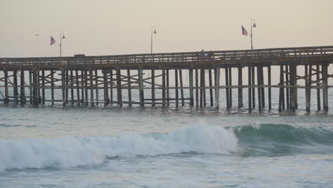 panning shot of huge waves rolling though the pacific ocean along ventura pier as the sun sets in the background located in southern california