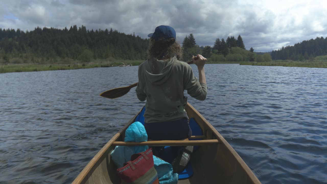 A woman sits in a canoe paddling down a river with forest in the background