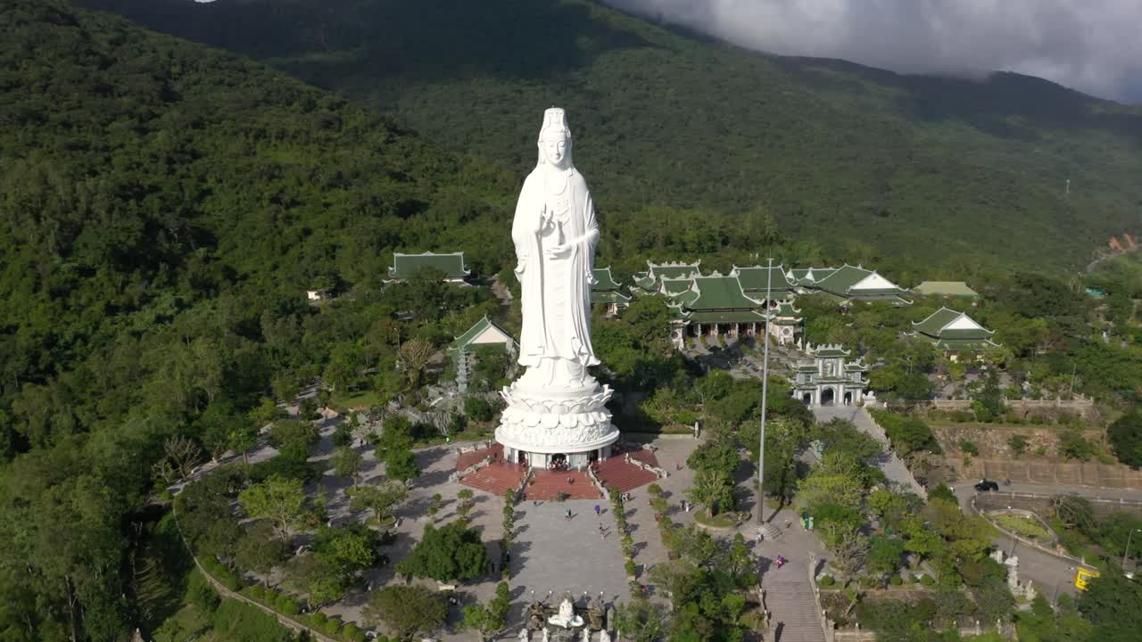 antena cercana dando vueltas alrededor de la estatua de buda y templos con enormes montañas y océano en da nang, vietnam