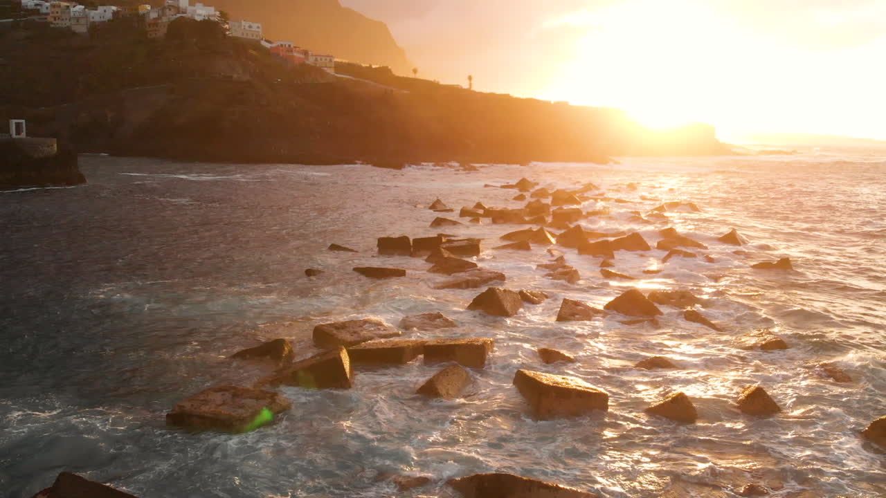 Vista laterale di una ripida costa vulcanica al tramonto, scogliere di lava vulcanica, oceano in tempesta, schiuma bianca dalle onde giganti che si infrangono sulle rocce. Ripresa aerea. Garachico, Tenerife, Isole Canarie