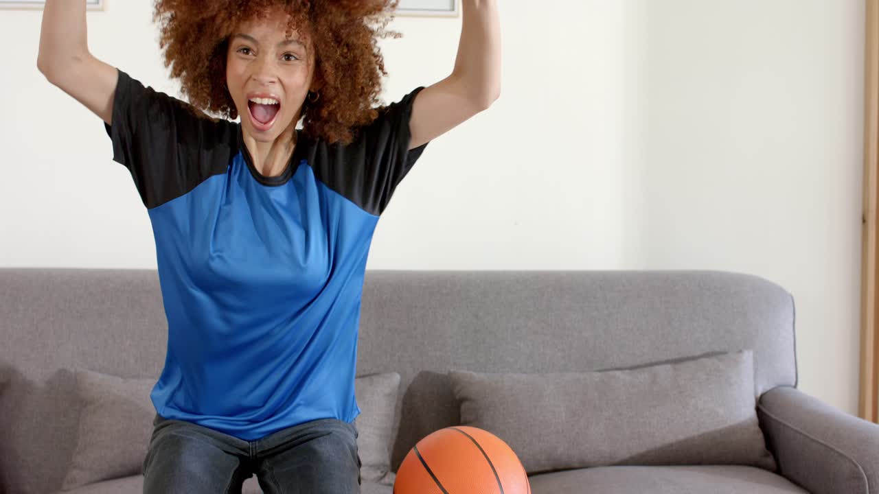 African American woman after rotating basketball reacting to surprise and cheering on grey sofa