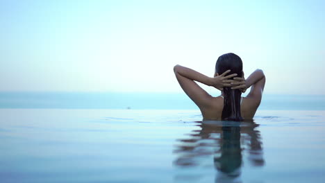 mujer joven emerge de la piscina infinita. camara lenta