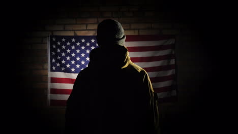 The-Silhouette-Of-A-Man----He-Looks-At-The-American-Flag-On-The-Brick-Wall-The-View-From-Behind