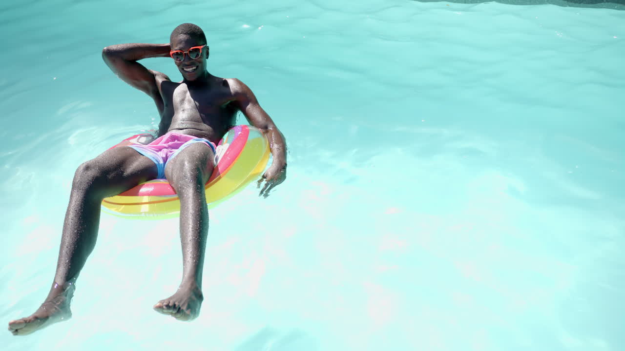 Relaxing on inflatable pool float, african american man wearing sunglasses enjoying sunny day, copy