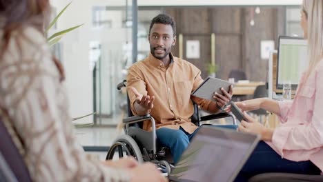 Disabled-diverse-businessman-in-wheelchair-using-tablet-with-colleagues-and-talking-in-slow-motion