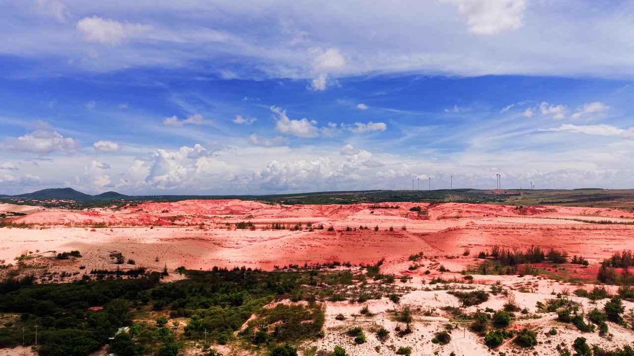 A vasta paisagem de Hoa Thang em Lam Dong. O sol brilha intensamente enquanto a terra apresenta solo vermelho, vegetação e nuvens em um céu azul.