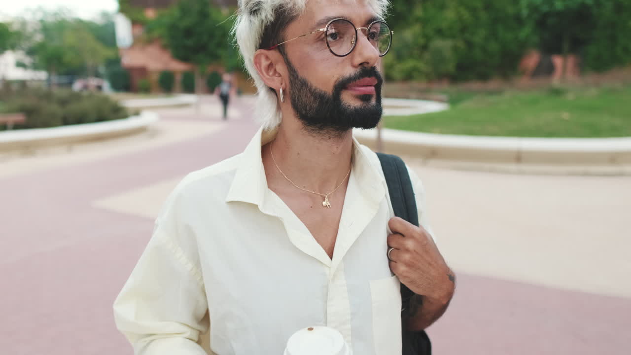 Giovane uomo con capelli decolorati e barba che cammina in un parco urbano