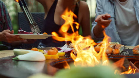 blonde woman using forceps on backyard. friends preparing fish and vegetables