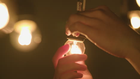 close up shot of a hand screwing a small hanging light bulb and turning it on