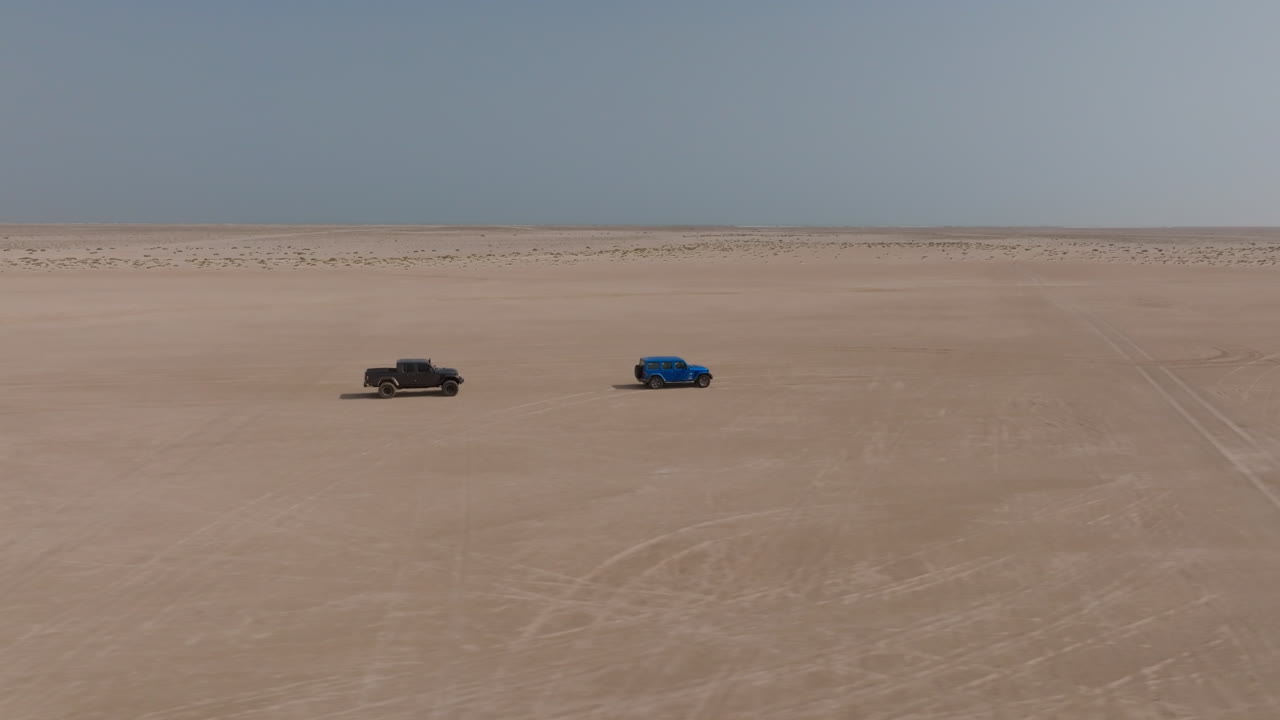 Two off-road cars driving across a flat desert near Bar Al Hikman, Oman