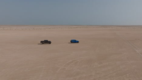 two off-road cars driving across a flat desert near bar al hikman, oman