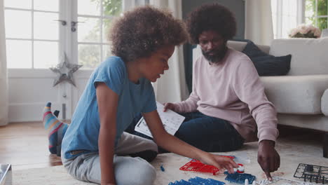 middle aged black father sitting on the floor at home helping his pre teen son with the instructions for a toy construction kit, close up, low angle