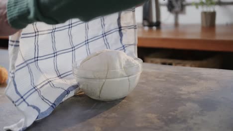 hands of caucasian man uncovering bread dough in kitchen, slow motion