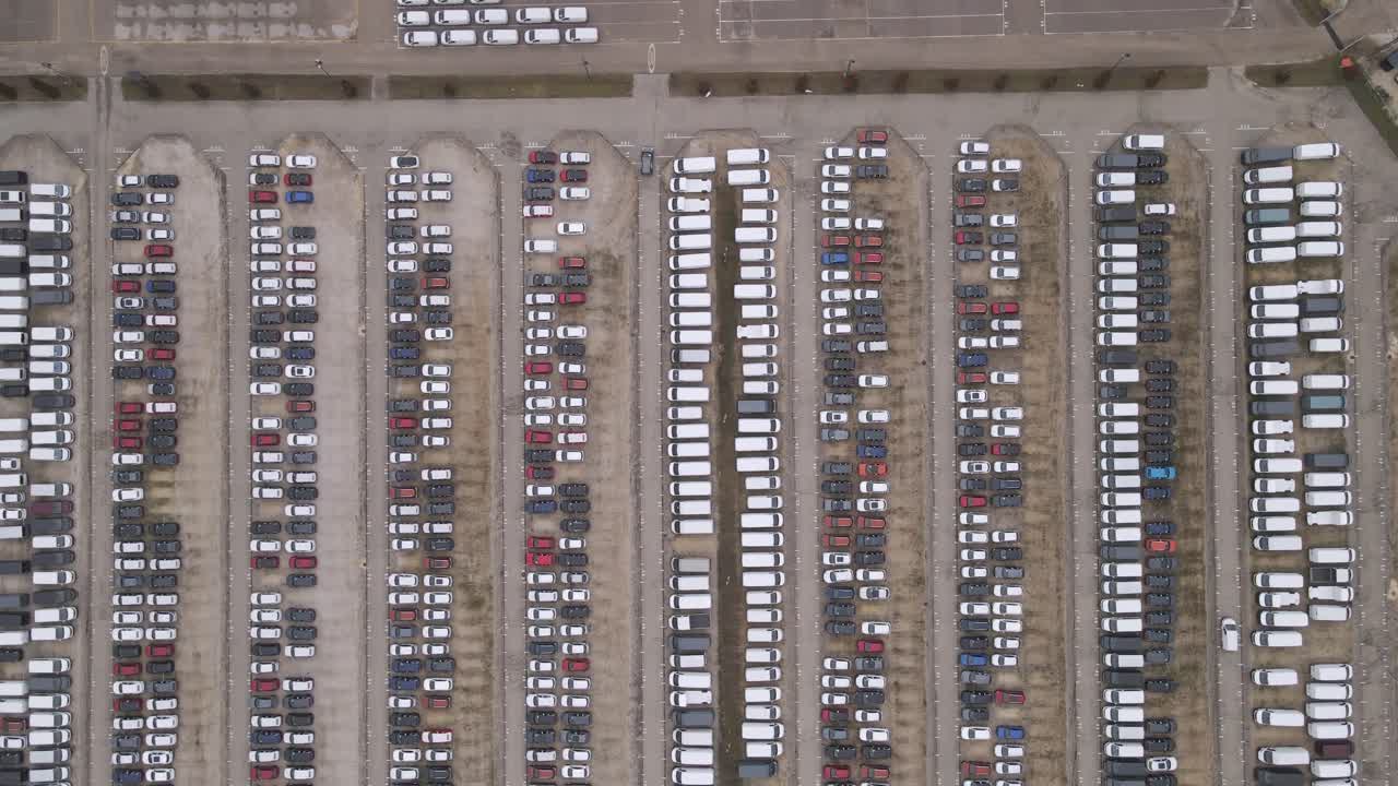 Aerial video of organized parking lot with vehicles, while cars leaving the area between the parking cars.