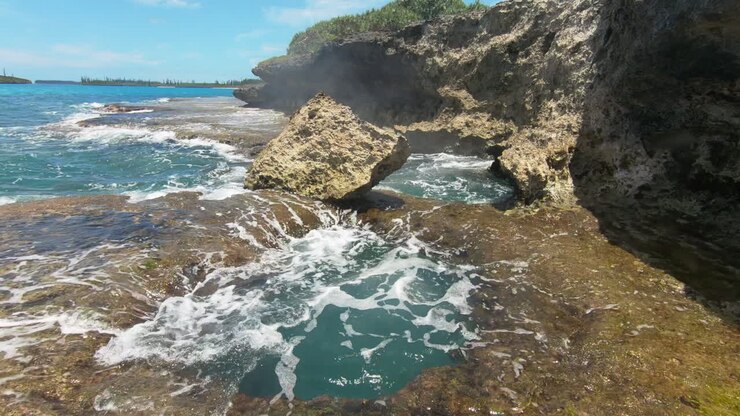 Vista aerea circolare di onde che escono da un foro roccioso, sulla costa dell'Isola dei Pini, Nuova Caledonia - ripresa con drone