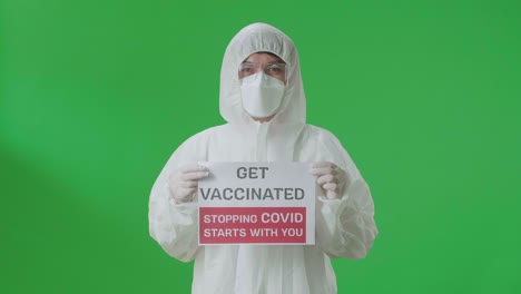 asian man wearing personal protective equipment uniform ppe, medical face mask and holding get vaccinated stopping covid starts with you sign in the green screen studio