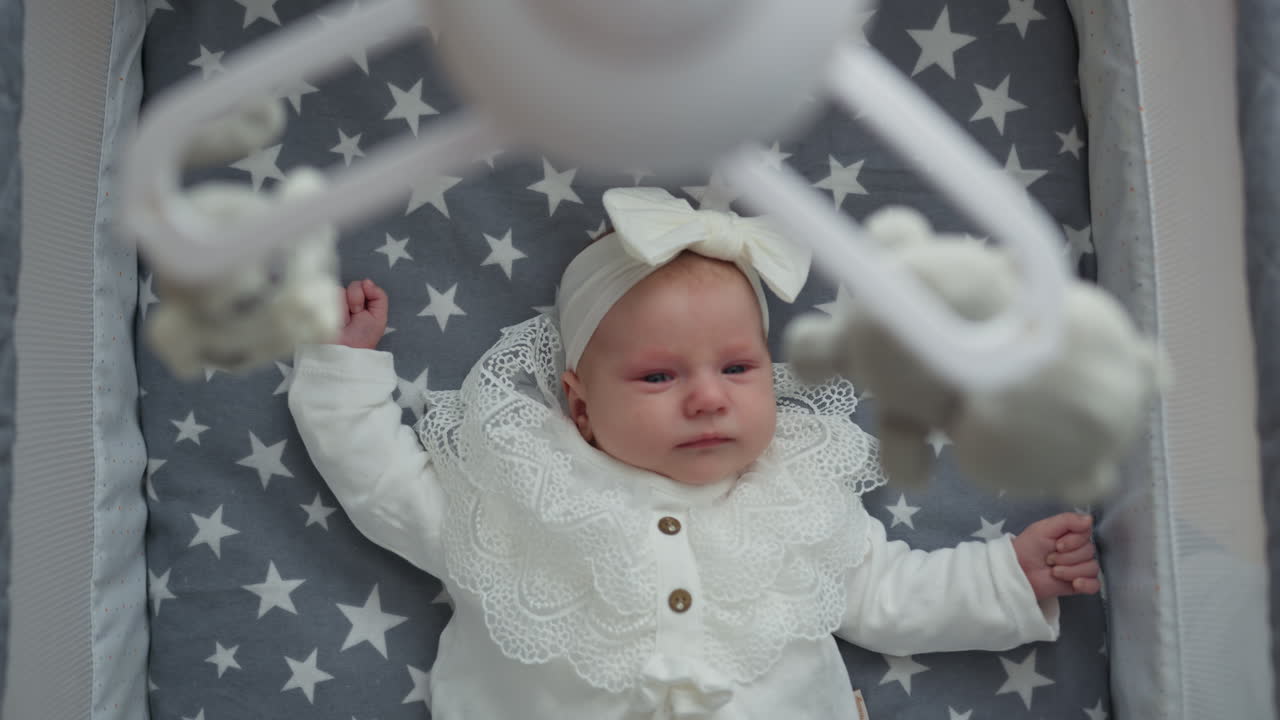 Neonato sdraiato nella culla che guarda un giocattolo mobile, bambino che riposa in una accogliente cameretta con giocattoli appesi
