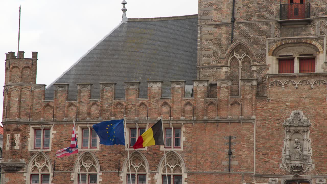 Flags flutter in wind on medieval brick facade, overcast daylight, static medium telephoto shot