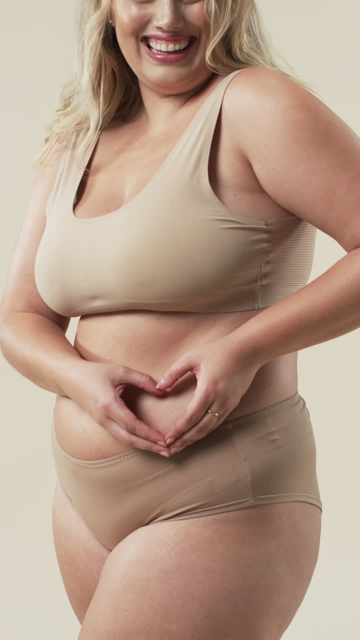 Video verticale: Donna curvy sorridente in intimo che forma un cuore con le mani, che abbraccia la body positivity.