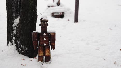personaje de lata oxidada sentado en la nieve junto a un árbol en un día de nieve en medio del invierno