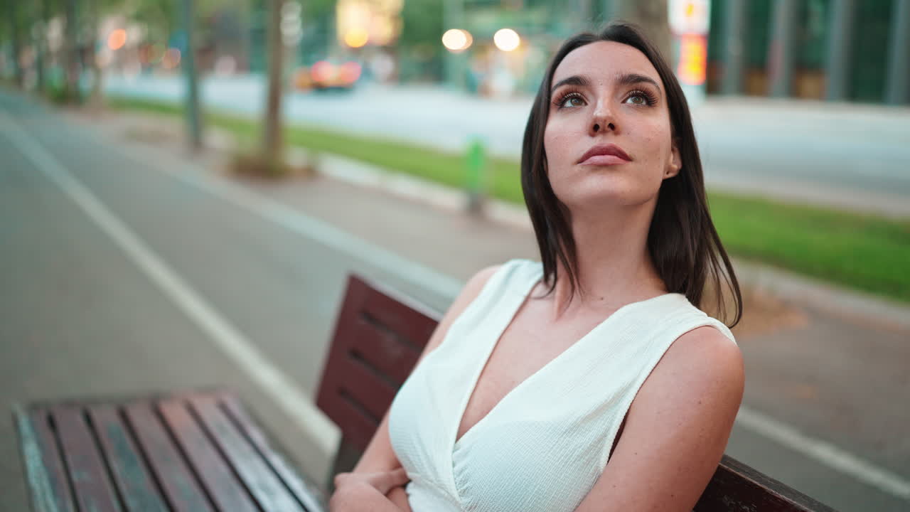 Žena v bílých šatech sedí na lavičce ve městě