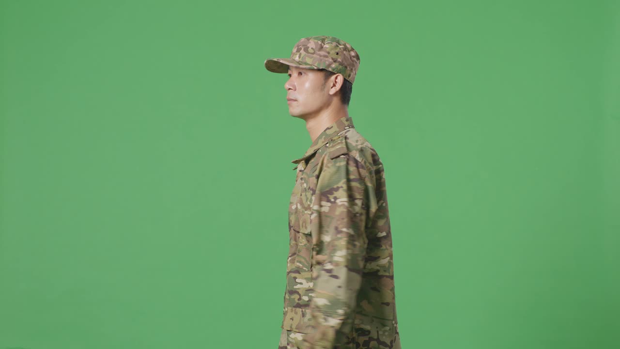 vista lateral del hombre asiático soldado caminando y mirando a su alrededor en la pantalla verde estudio de fondo