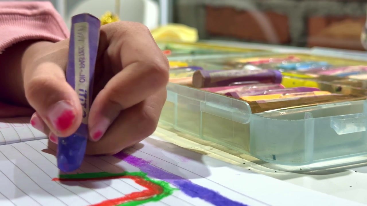Mão de criança colorindo com giz de cera no papel, caixa de giz de cera colorida por perto, criatividade infantil e atividade artística.