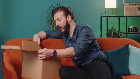 happy lebanese man shopper unpacking cardboard box delivery parcel online shopping purchase at home