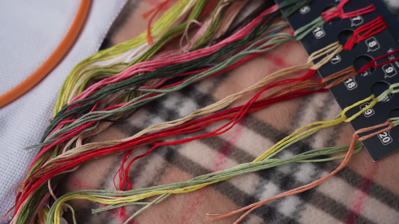 부드러운 체크무늬 담요 위에 놓인 다채로운 자수 실의 클로즈업 사진이에요. 바느질, 자수, 수공예 준비에 사용되는 생생한 털실 색상의 혼합과 텍스처 디테일을 보여주고 있어요.