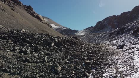 Aerial-climbs-snowy-talus-scree-slope-in-alpine-mountains,-Argentina