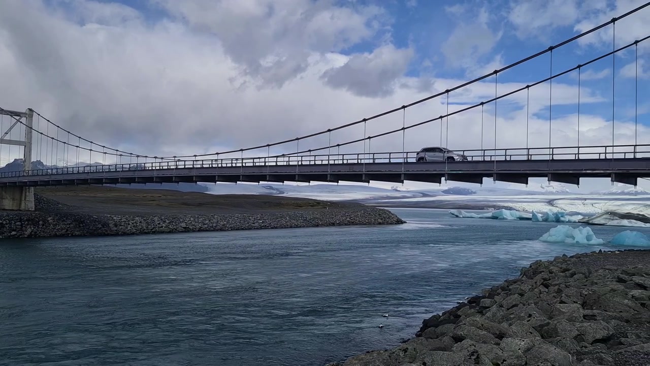 Auto che si muove su un ponte sopra il deflusso di un fiume da un lago glaciale in un paesaggio islandese