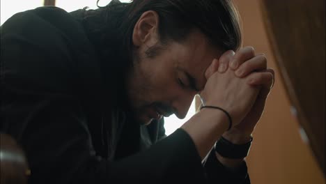 young man in black suit praying in church in cinematic slow motion