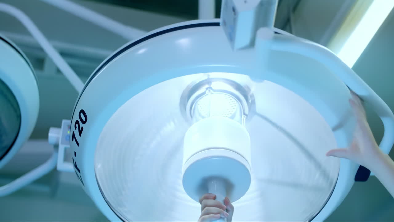병원 수술실 그림자 없는 조명 시설, 스크럽 간호사 손 바닥 스탠드에 수술 led 조명을 켜고, 램프가 천천히 켜지고, 의료 직원이 작동하는 현대 의료 장비