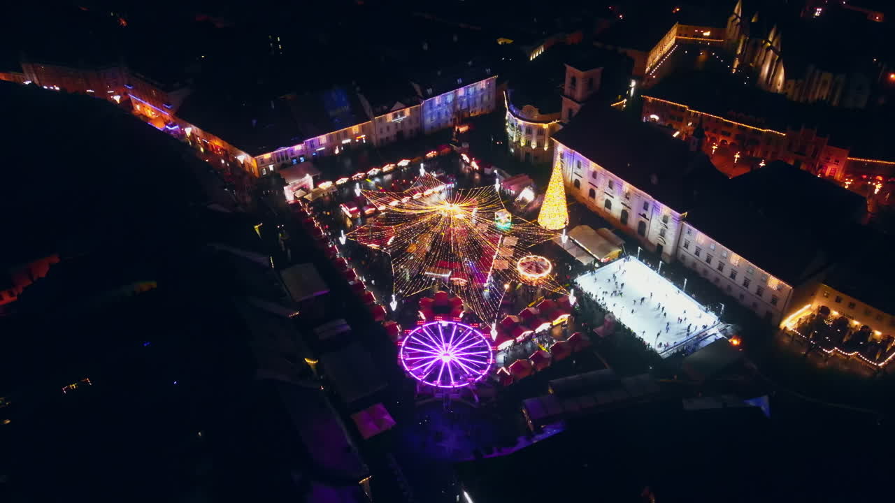 Aerial drone view of The Big Square in Sibiu at night, Romania. Old city centre decorated for Christmas. Ferris wheel, skating rink, cityscape, people