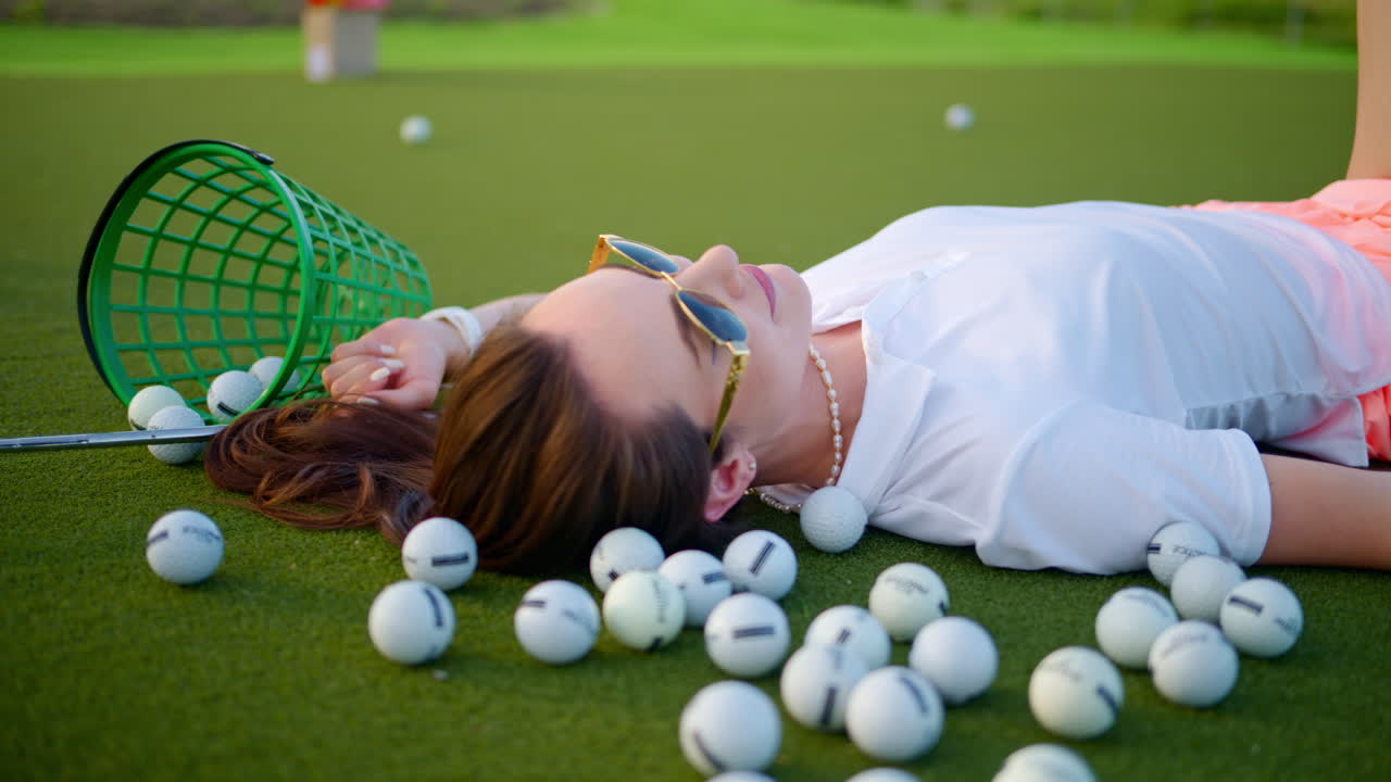 Donna sdraiata sul campo da golf vicino a un secchio con palline rovesciate