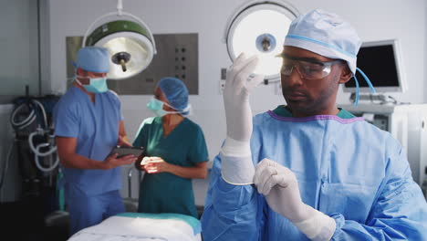 portrait of male surgeon wearing scrubs putting on latex gloves in hospital operating theater