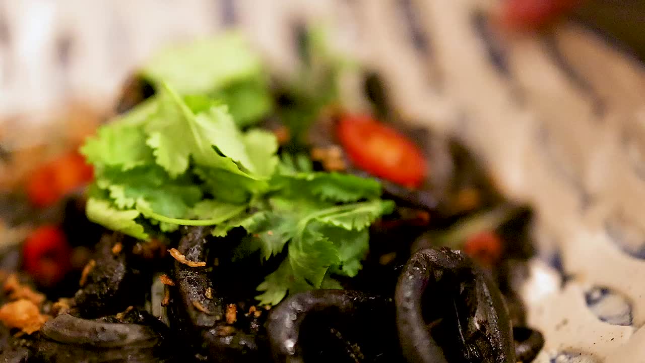 Close-up of squid rings garnished with cilantro and red chili slices on a patterned plate.