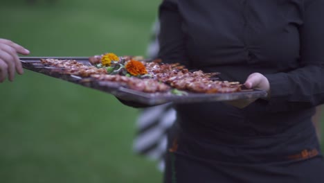 Female server in black outfit offering meat skewers to event&#039;s guests