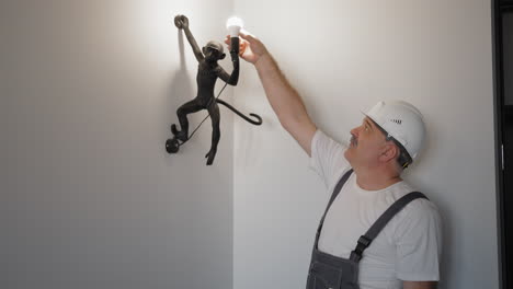 electrician inserts and checks the operation of the light bulb in the luminaire