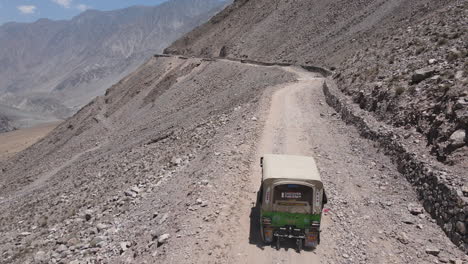 Vista-Aérea-De-Un-Camión-Que-Se-Mueve-Por-Un-Camino-De-Tierra-En-Las-Montañas-De-Pakistán,-Disparo-De-Un-Dron