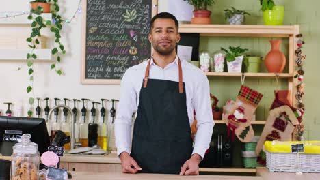 frente a la cámara hombre negro carismático barista posando frente a la camera en la cafetería él cruzando las manos y sonriendo un poco. tiro en arri alexa mini.