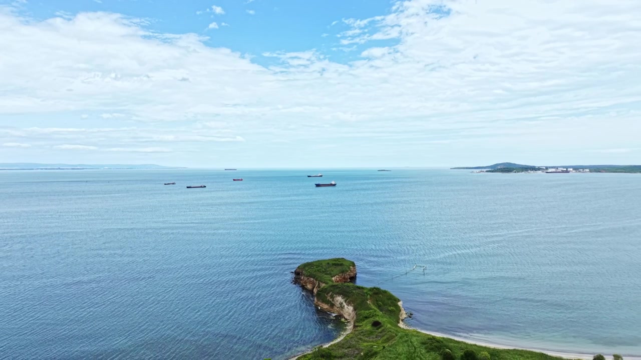 ทิวทัศน์ทะเลที่สงบพร้อมเรือบรรทุกสินค้าที่ขอบฟ้าและเกาะที่ปกคลุมด้วยหญ้าในเวลากลางวันภายใต้ท้องฟ้าสีครามที่มีเมฆ