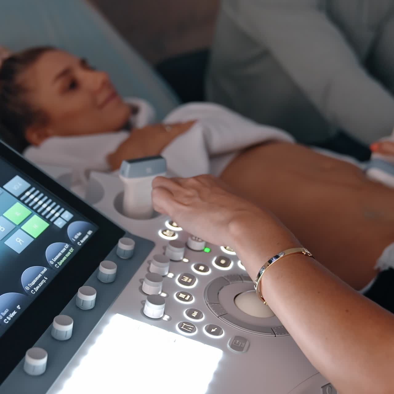 Doctor's hand operating ultrasound machine for pregnant lady examination. Medic moves the sensor by the belly of Caucasian woman