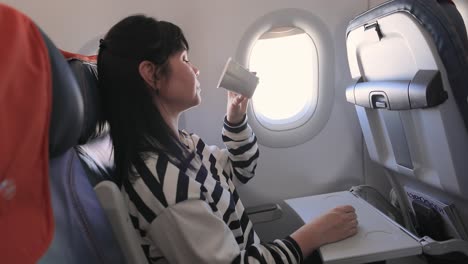 woman sitting inside airplane and looking at window and drinks coffee.