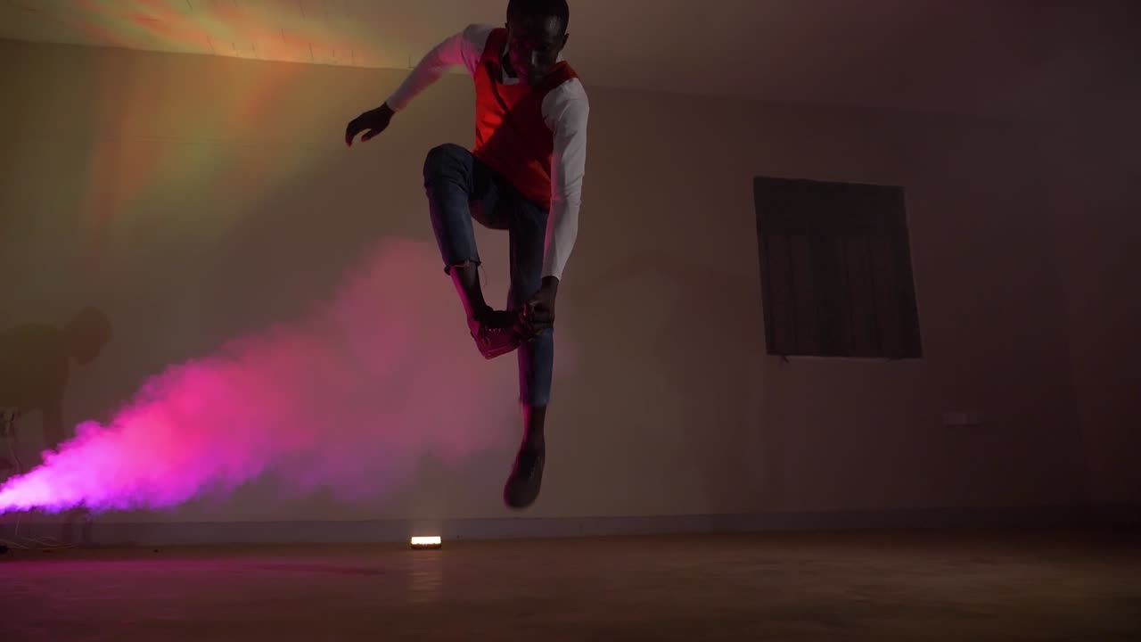 toma en cámara lenta de jóvenes africanos con una camisa roja haciendo un truco de salto con las piernas en luces de discoteca coloridas y humo