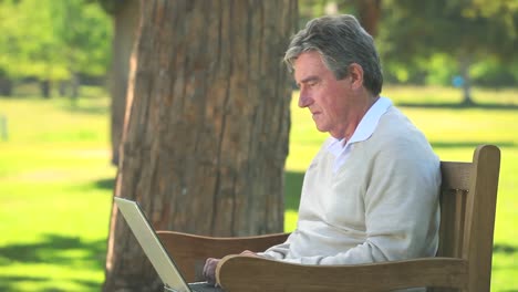 Elderly-man-using-his-laptop-on-a-bench
