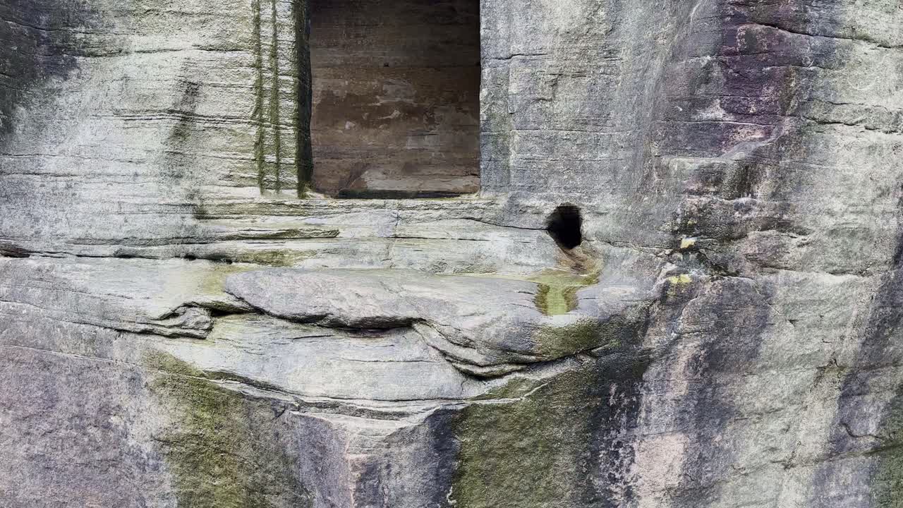 A tilt-up shot reveals a weathered cave entrance carved into stone, highlighting its rough textures, natural erosion, and architectural simplicity